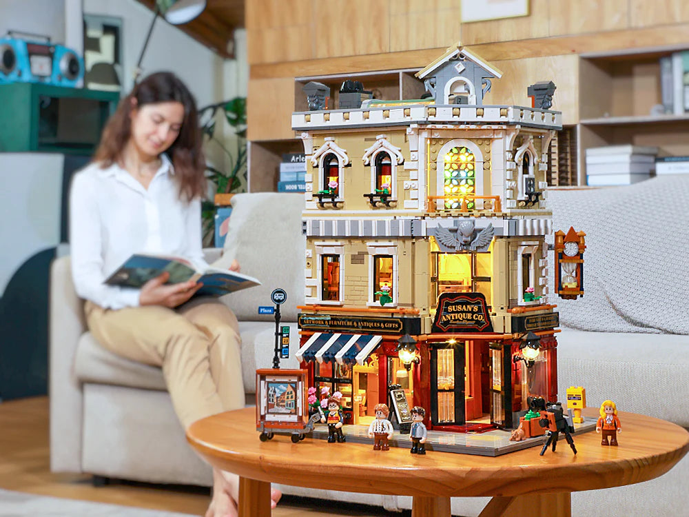Illuminated Funwhole Antique Store building set displayed on a table, with a woman reading in the background.