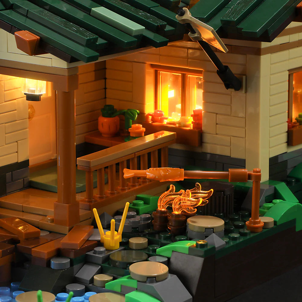 Close-up of Funwhole Lakeside Lodge set showing a cozy campfire with fish roasting, a porch, and warm glowing windows