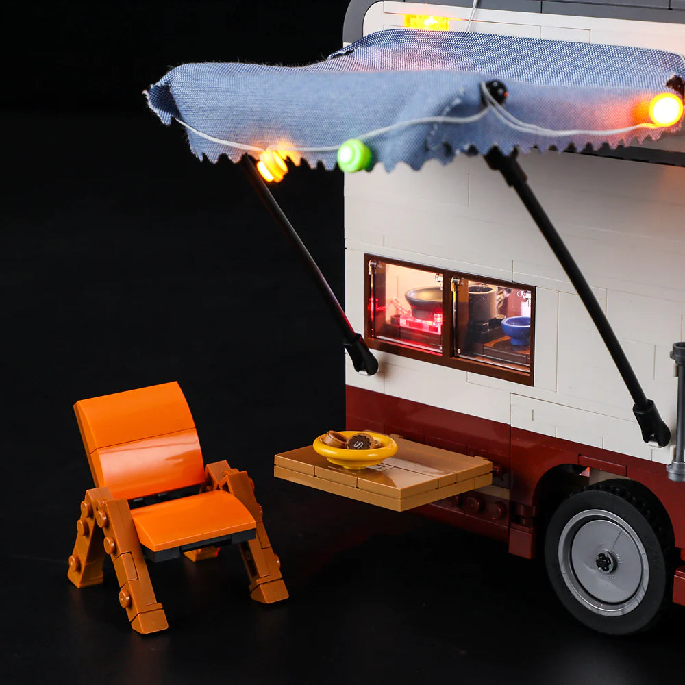 Lumibricks F9012 Camper Van exterior with blue awning, orange chair, fold-out table, and string LED lights at night