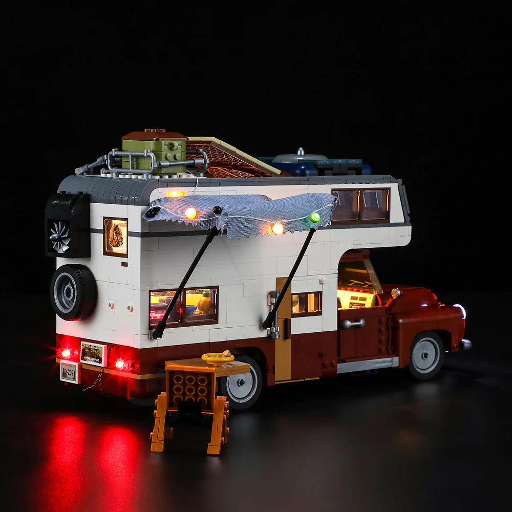Lumibricks F9012 Camper Van with open side door, extended awning with string lights, and outdoor table at night