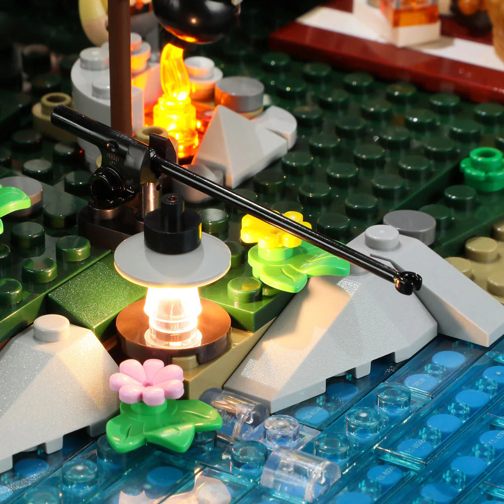 Lumibricks F9022 Lookout Campground close-up of fishing rod, glowing lantern, flowers, rocks, and campfire by the water