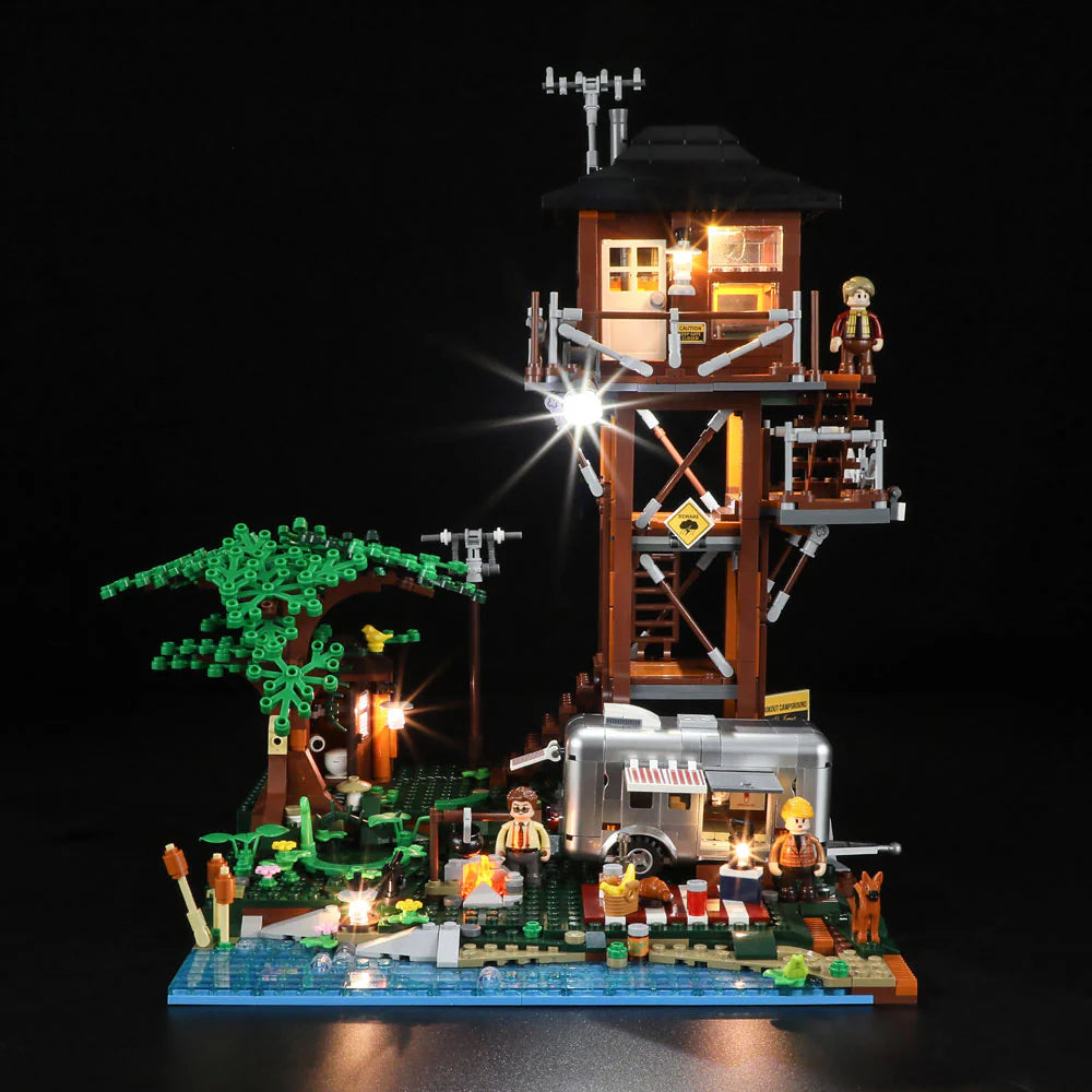 Front view of Lumibricks F9022 Lookout Campground at night, showing lit tower, camper trailer, campfire, tree, minifigures, and dog