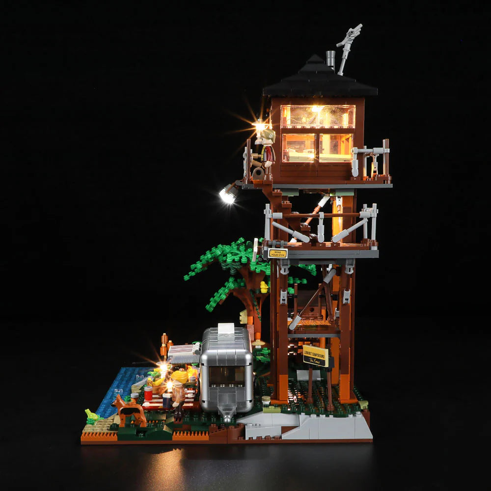 Side view of Lumibricks F9022 Lookout Campground at night, featuring illuminated lookout tower, camper trailer, tree, figures, and dog