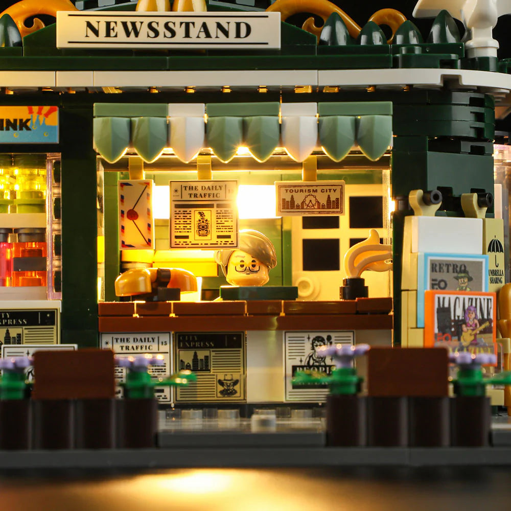 Lumibricks F9023 Newsstand front view at night with glowing interior, vendor at counter, and printed newspapers and magazines