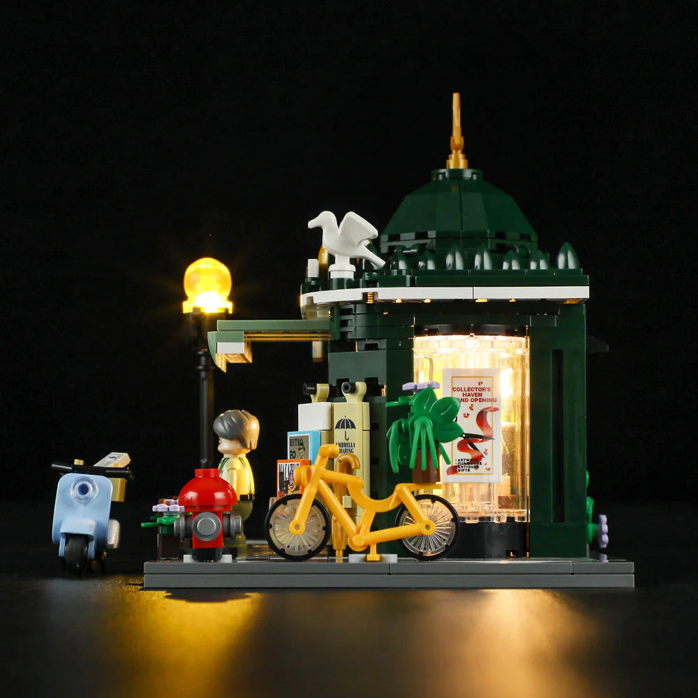Lumibricks F9023 Newsstand at night with illuminated dome, minifigure vendor, yellow bicycle, scooter, and street lamp