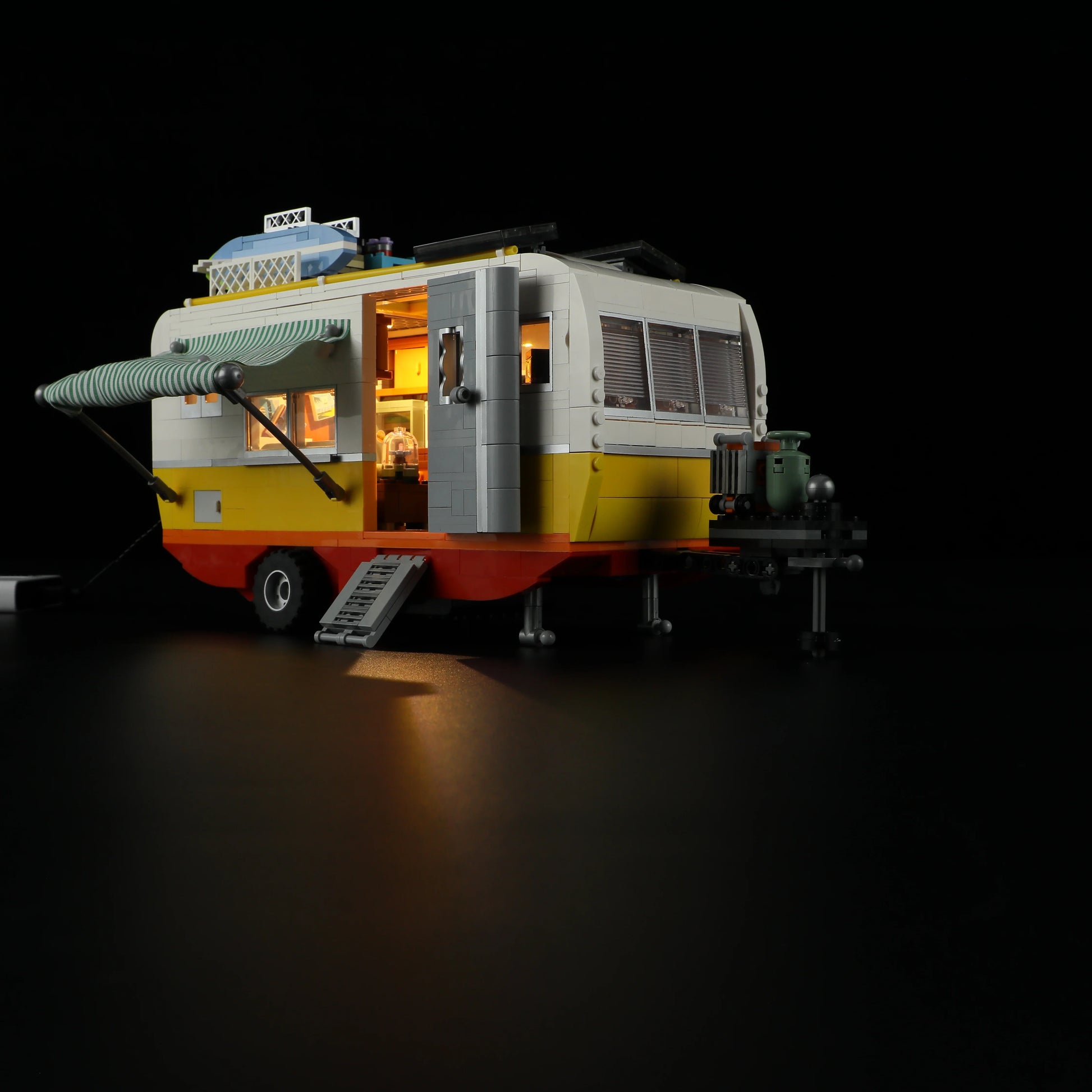 Lumibricks F9032 Travel Trailer angled night view with open door, lit interior, and rooftop surfboards