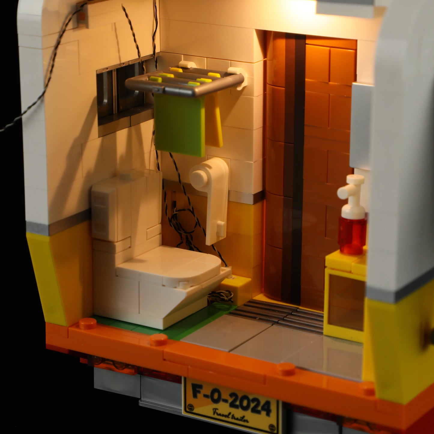 Lumibricks F9032 Travel Trailer bathroom interior with toilet, towel rack, soap dispenser, and warm lighting