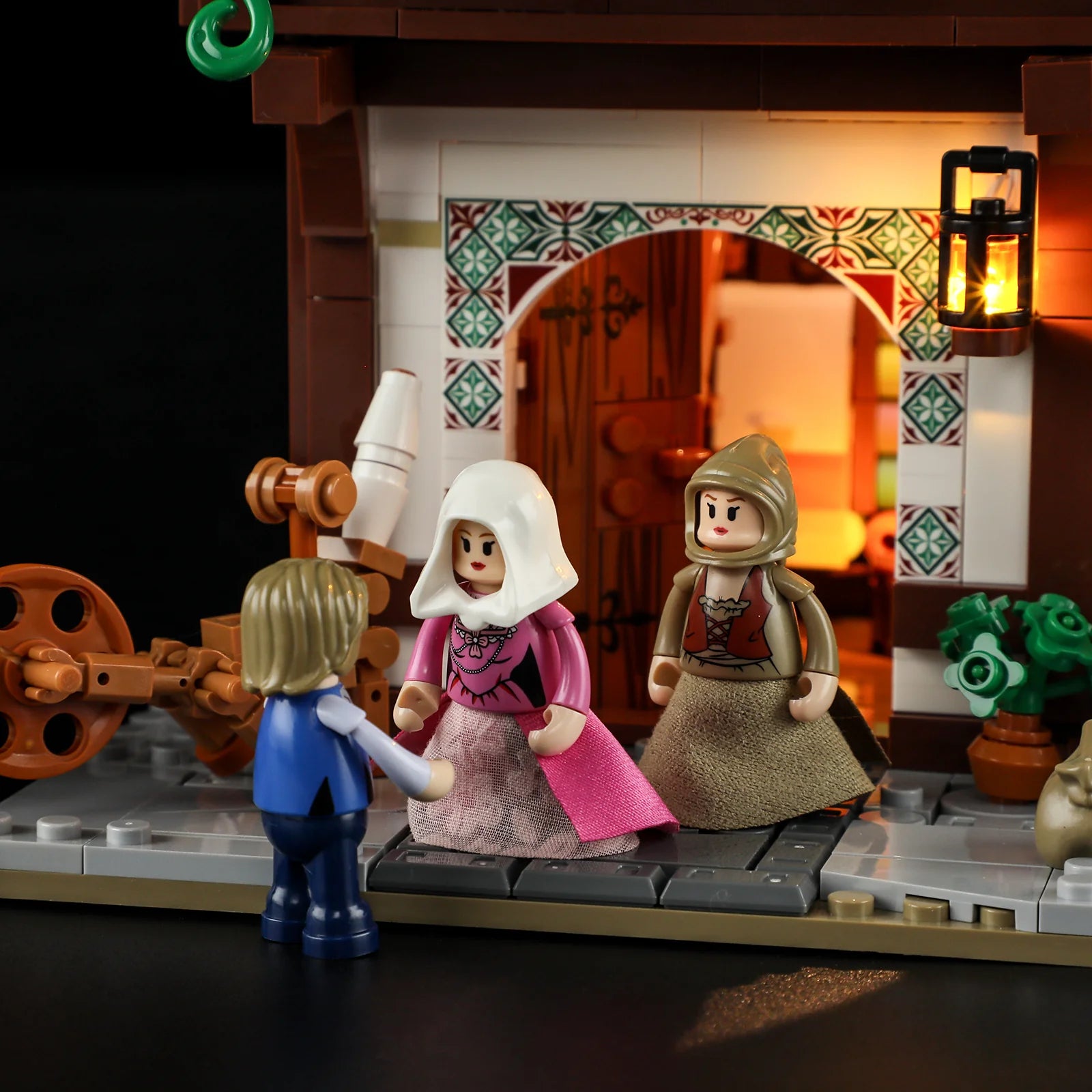 Lumibricks F9038 Medieval Tailor Shop entrance at night with customers, medieval outfits, spinning wheel, and glowing lantern