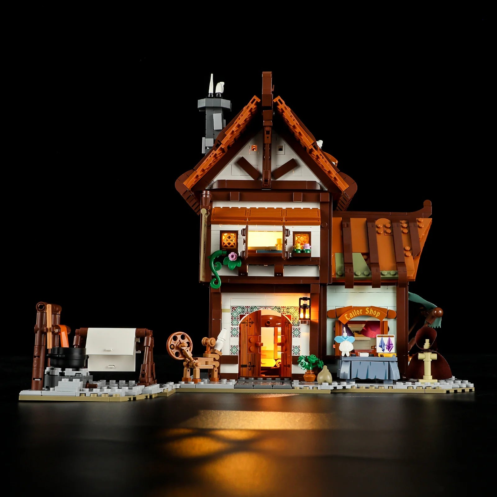 Lumibricks F9038 Medieval Tailor Shop front view at night with glowing LED lights, wooden roof, and illuminated entrance