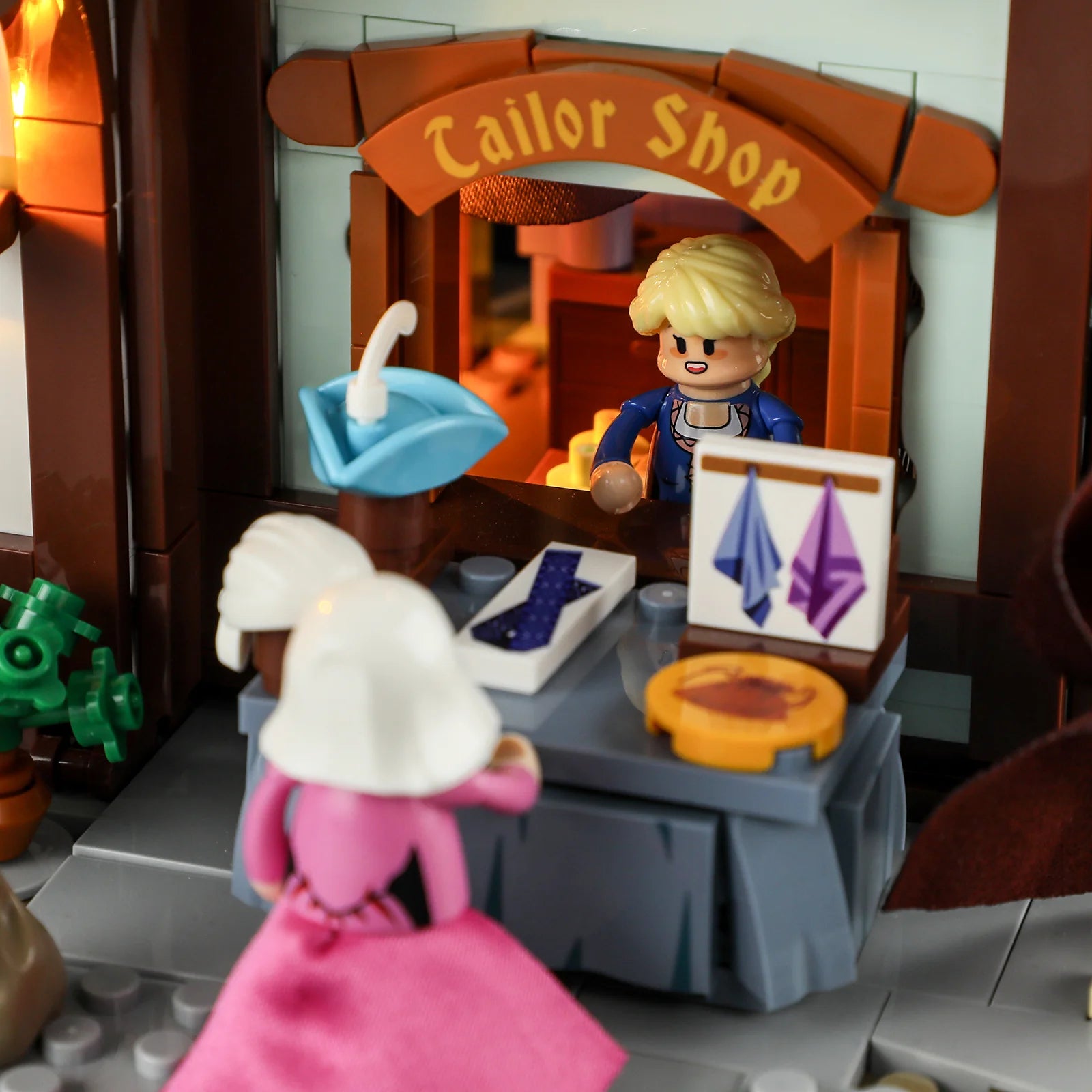 Lumibricks F9038 Medieval Tailor Shop exterior sales window with tailor, market display, hats, scarves, and illuminated sign