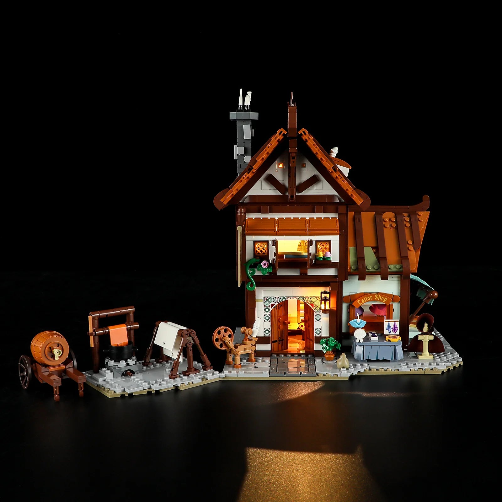 Lumibricks F9038 Medieval Tailor Shop side angle at night with market stall, sewing station, and warm LED lighting